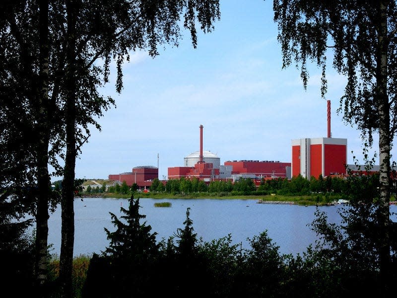 The a cluster of red and grey buildings in the unfinished Olkiluoto-3 nuclear reactor in Eurajoki, Finland, as seen through a clearing in a forest.