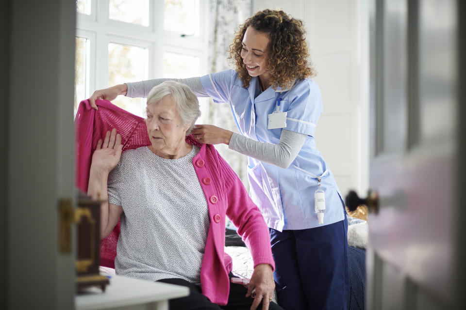 home carer helping senior woman get dressed in her bedroom