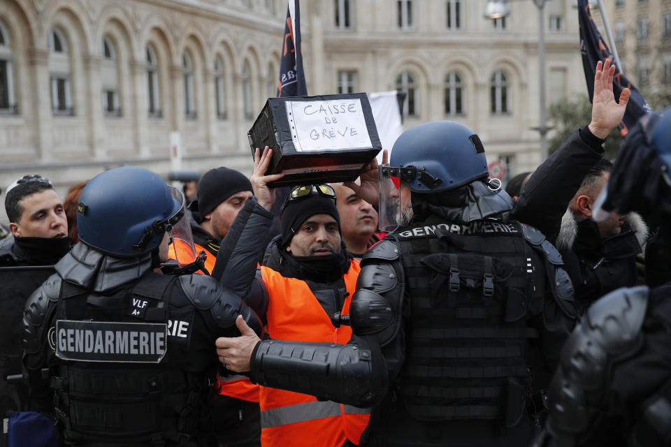 A striking train worker holds a box to collect -funds for striking workers in front of riot police officers outside the the Gare de Lyon train station, Monday, Dec. 23, 2019 in Paris. A wildcat protest comes on Day 19 of nationwide strike over the government's plans to raise the retirement age to 64. The union-led protest Monday led to a standoff with riot police that spilled onto the streets around the historic Gare de Lyon train station. (AP Photo/Francois Mori)