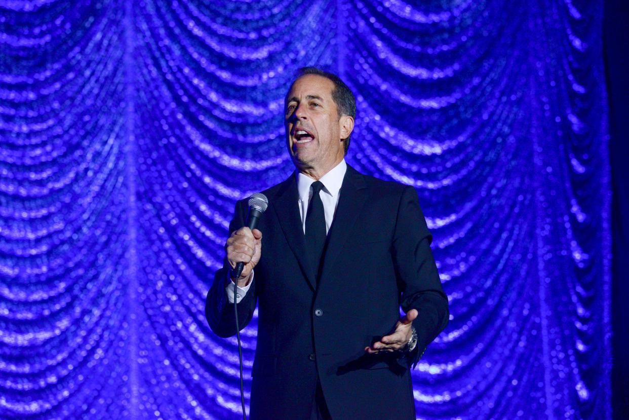 Comedian Jerry Seinfeld holding a microphone.