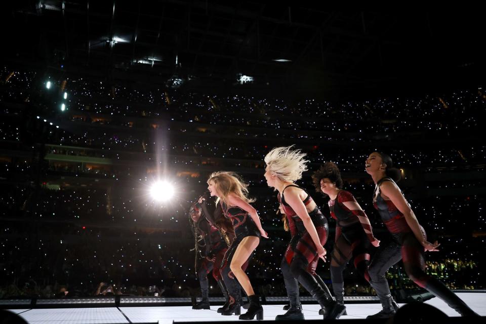 Taylor Swift and dancers lean forward on stage at SoFi Stadium in front of the crowd.