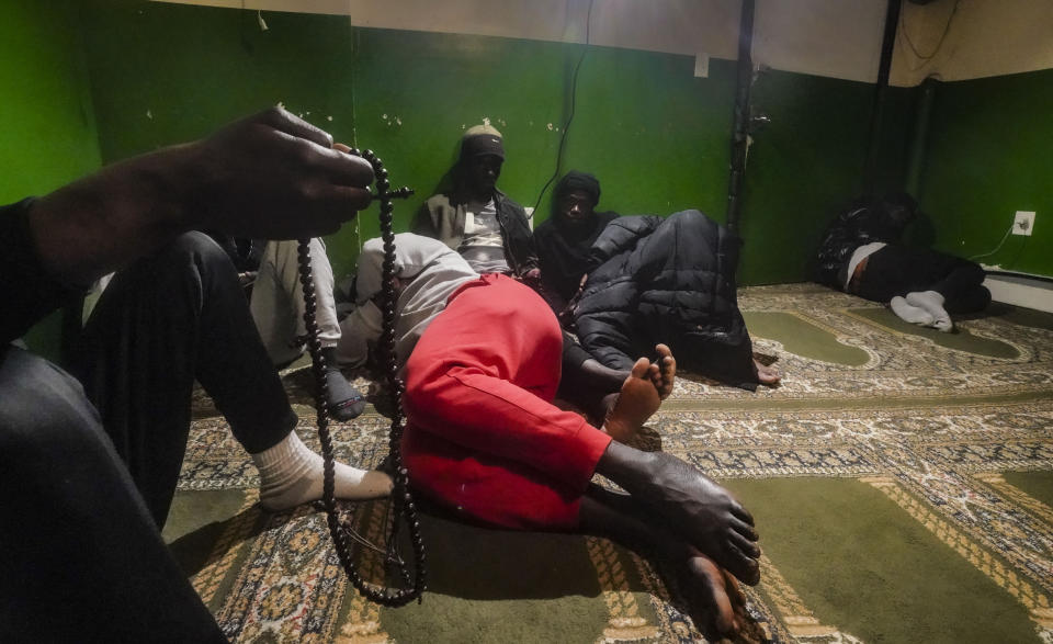 HOLD FOR STORY BY PHILIP MARCELO - A Senegalese migrant, left, holds a Muslim prayer bead following morning prayers, while other African migrants rest inside the main prayer area in the basement at Bronx's Masjid Ansaru-Deen mosque, Friday March 15, 2024, in New York. The mosque, formerly the family home for its Imam Omar Niass, has served as a temporary shelter and refuge since 2020 for hundreds of African migrants, while seeking asylum in the United States. (AP Photo/Bebeto Matthews)