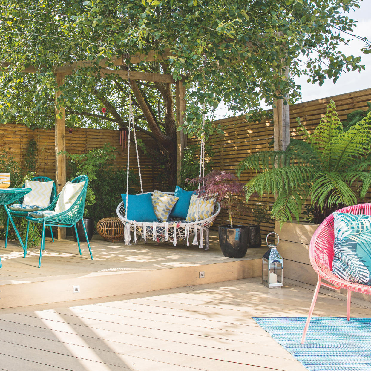  Patio cover ideas, split level decking with bright furniture, hanging garden seat in corner under tree . 