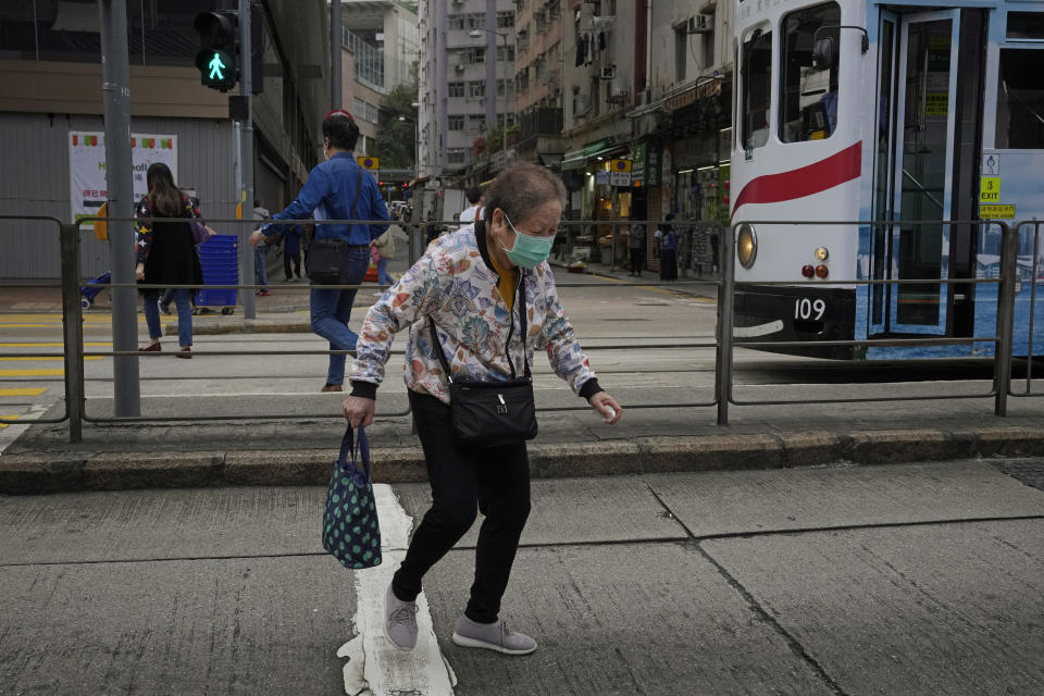 An elderly woman wearing a face mask walks alone a street in Hong Kong, Sunday, March 13, 2022. The territory's leader, Chief Executive Carrie Lam, warned the peak of the latest surge in coronavirus infections might not have passed yet. (AP Photo/Kin Cheung)