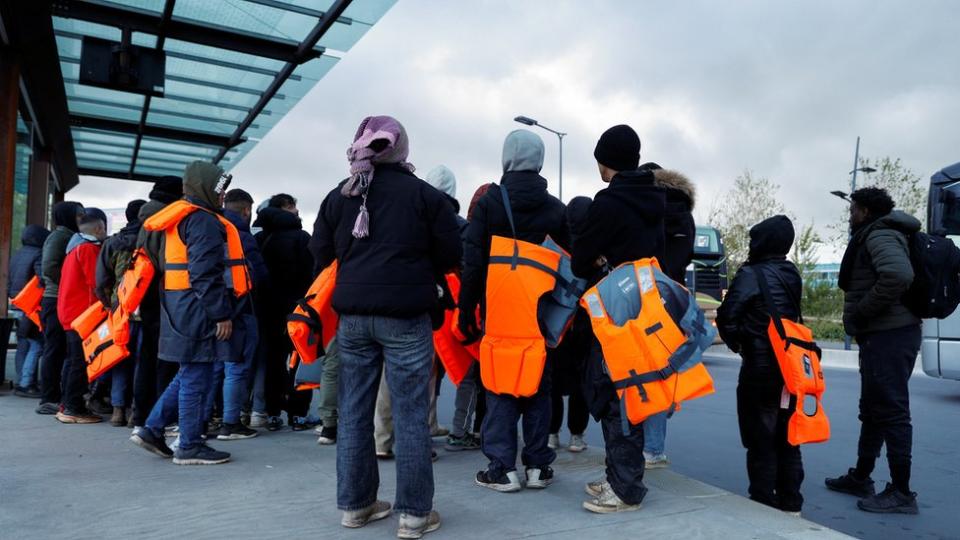 Migrants wait for a bus to return from the beach to their camp in Calais after people died trying to cross the English Channel on Tuesday