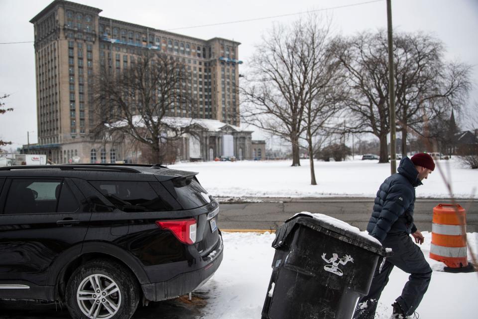 With the Michigan Central Station in the background, Stephen McGee  of Detroit takes the trash can out to the curb outside his home in Corktown in Detroit Feb. 18, 2021.