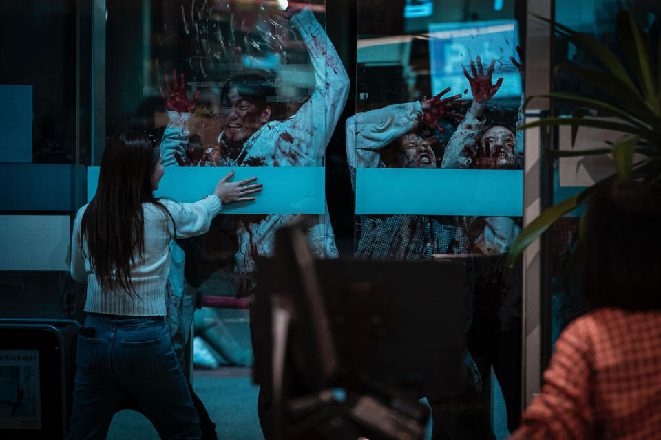 a woman holds closed a glass door with zombies behind it on zombieverse netflix