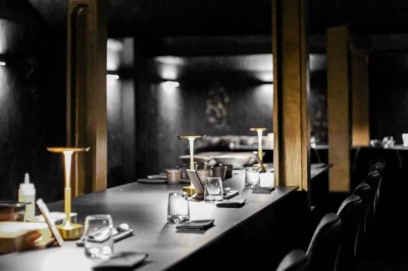 Interior shot of Andrew Sheridan's restaurant in Liverpool with grey and black walls, grey tables, and gold beams