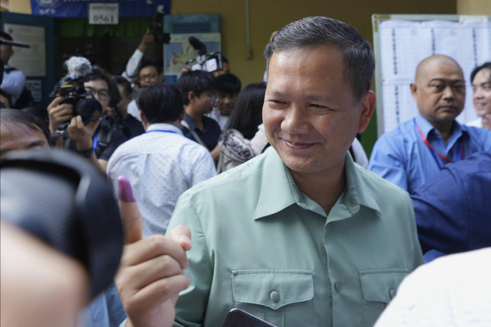 Hun Manet, center, of the Cambodian People's Party (CPP), son of Cambodia Prime Minister Hun Sen, also army chief, shows off his inked finger outside a polling station after voting in Phnom Penh, Cambodia, Sunday, July 23, 2023. Hun Sen has suggested he will hand off the premiership during the upcoming five-year term to his oldest son, Hun Manet, perhaps as early as the first month after the elections. (AP Photo/Heng Sinith)