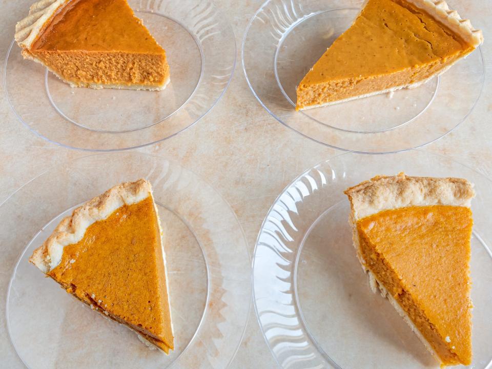 Four pumpkin-pie slices on clear plates on a counter