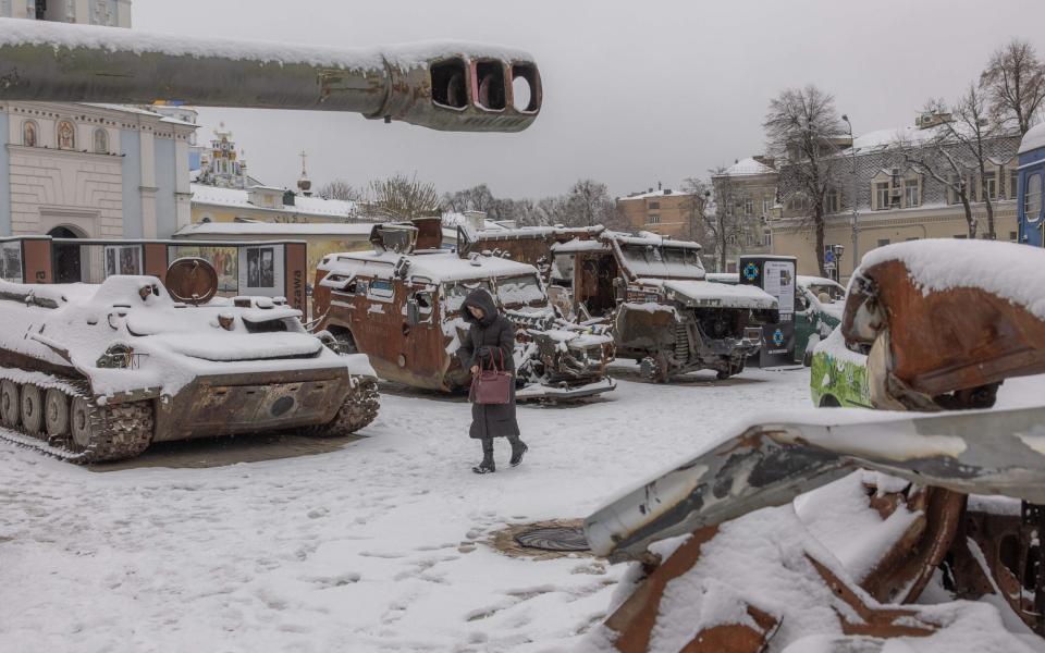 A woman walks past destroyed Russian military vehicles blanketed in snow in downtown Kyiv