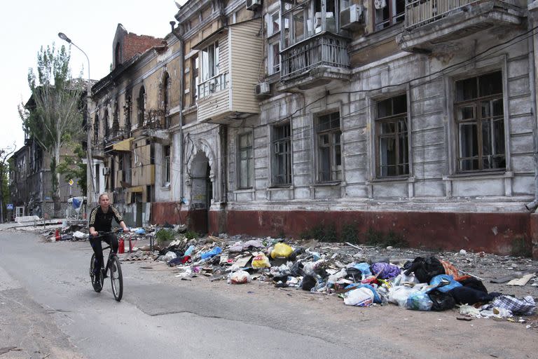 Una mujer pasa en bicicleta por delante de un edificio dañado durante los combates en Mariúpol el miércoles 25 de mayo de 2022, en el territorio bajo el gobierno de la República Popular de Donetsk, en el este de Ucrania. (Foto AP)