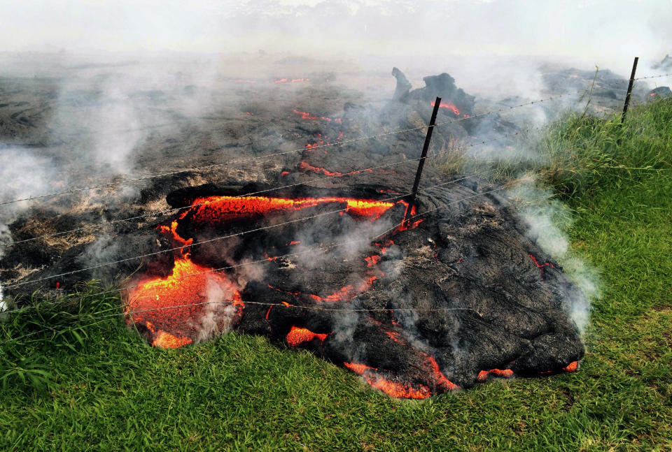 This Oct. 25, 2014 photo provided by the U.S. Geological Survey shows lava flow advancing across the pasture between the Pahoa cemetery and Apaa Street, engulfing a barbed wire fence, near the town of Pahoa on the Big Island of Hawaii. Dozens of residents in this rural area of Hawaii were placed on alert as flowing lava continued to advance. Authorities on Sunday, Oct. 26, 2014 said lava had advanced about 250 yards since Saturday morning and was moving at the rate of about 10 to 15 yards an hour, consistent with its advancement in recent days. The flow front passed through a predominantly Buddhist cemetery, covering grave sites in the mostly rural region of Puna, and was roughly a half-mile from Pahoa Village Road, the main street of Pahoa. (AP Photo/U.S. Geological Survey)