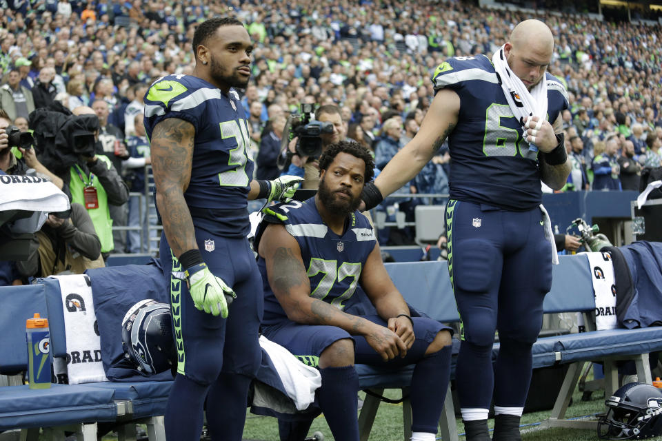 Seattle Seahawks defensive end Michael Bennett, center, is joined by teammates Thomas Rawls, left, and Justin Britt, as he sits during the singing of the national anthem. (AP)