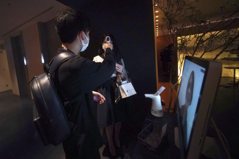 A restaurant employee, on monitor, remotely attends as customers check their temperatures before entering the restaurant as a measure against the new coronavirus prevention at Kichiri, an “izakaya” or Japanese style restaurant at Shinjuku district in Tokyo Thursday, June 4, 2020. As Japanese return to schools, shops and offices reconfigured to help prevent new coronavirus infections with ample use of plastic screens, masks and reminders to keep their distance, access to faster testing is crucial, officials say. (AP Photo/Eugene Hoshiko)