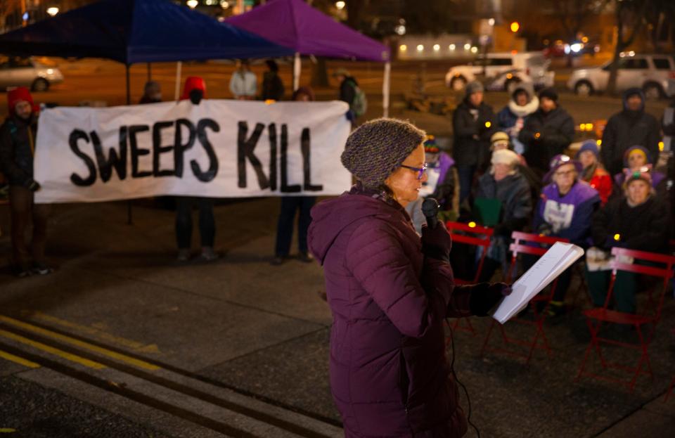 Eugene Mayor Lucy Vinis on Wednesday reads the names of people who died while experiencing homelessness in the community as a group holds a sign in protest of city sweeps during a candlelight vigil for National Homeless Persons' Remembrance Day in the Park Blocks of Eugene.
