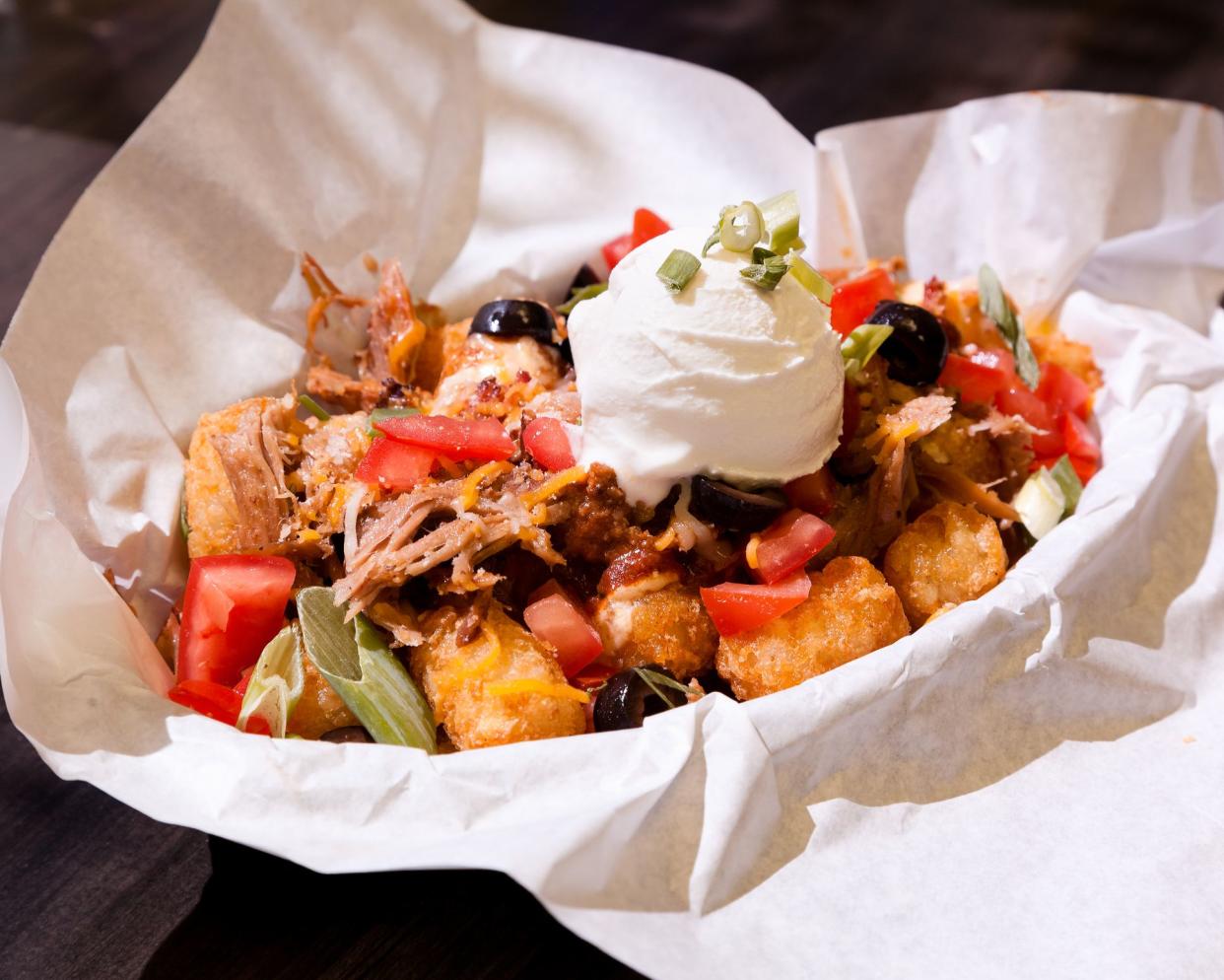 Tater tot nachos with pulled pork, sour cream, olives, and salsa.