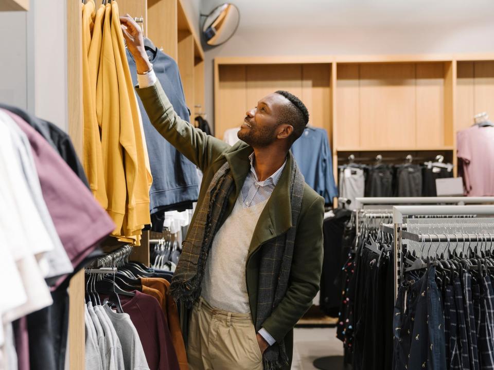 A man in a jacket picks out a sweater in a store.