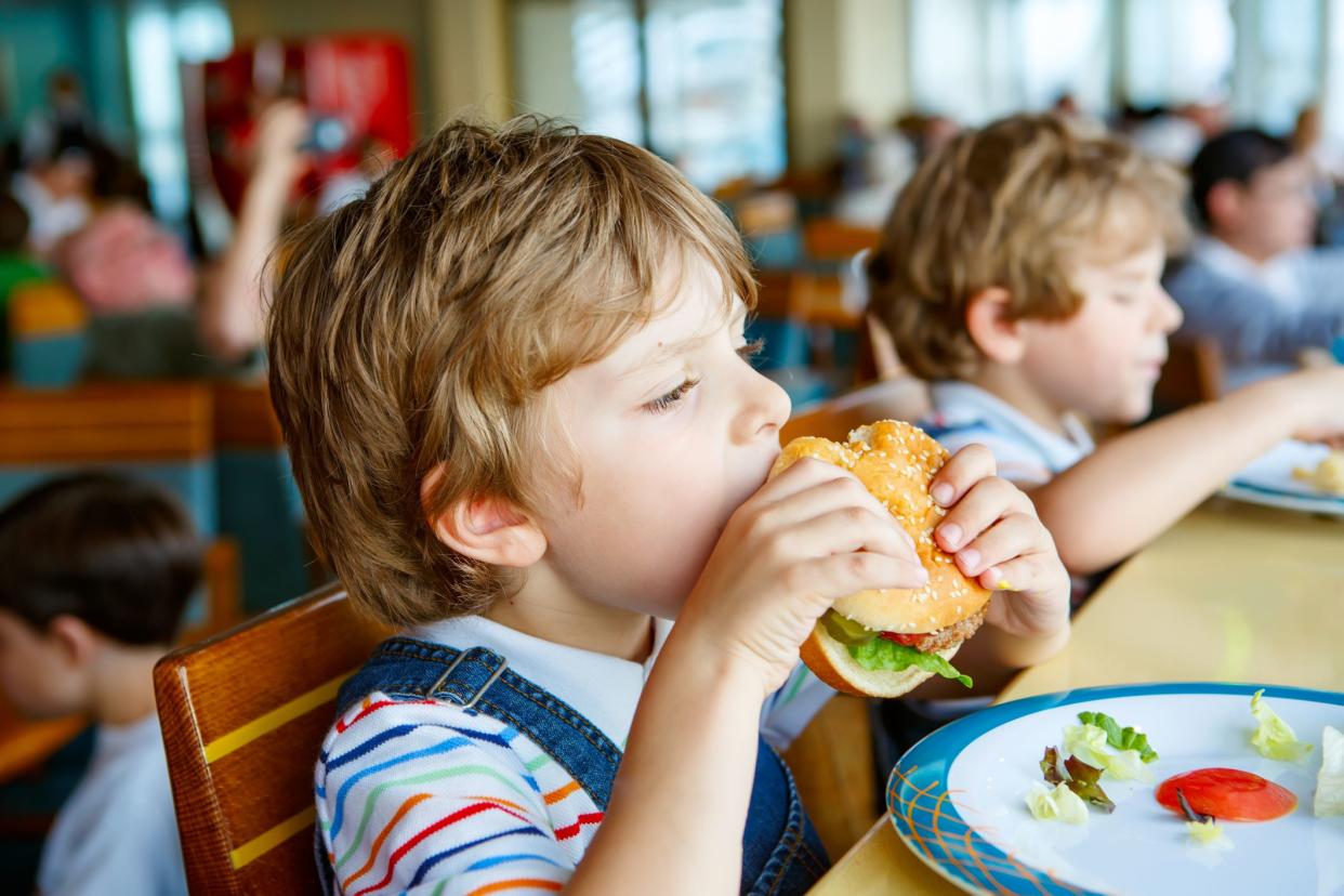 Cute healthy preschool kid boy eats hamburger sitting in school or nursery cafe. Happy child eating healthy organic and vegan food in restaurant. Childhood, health concept