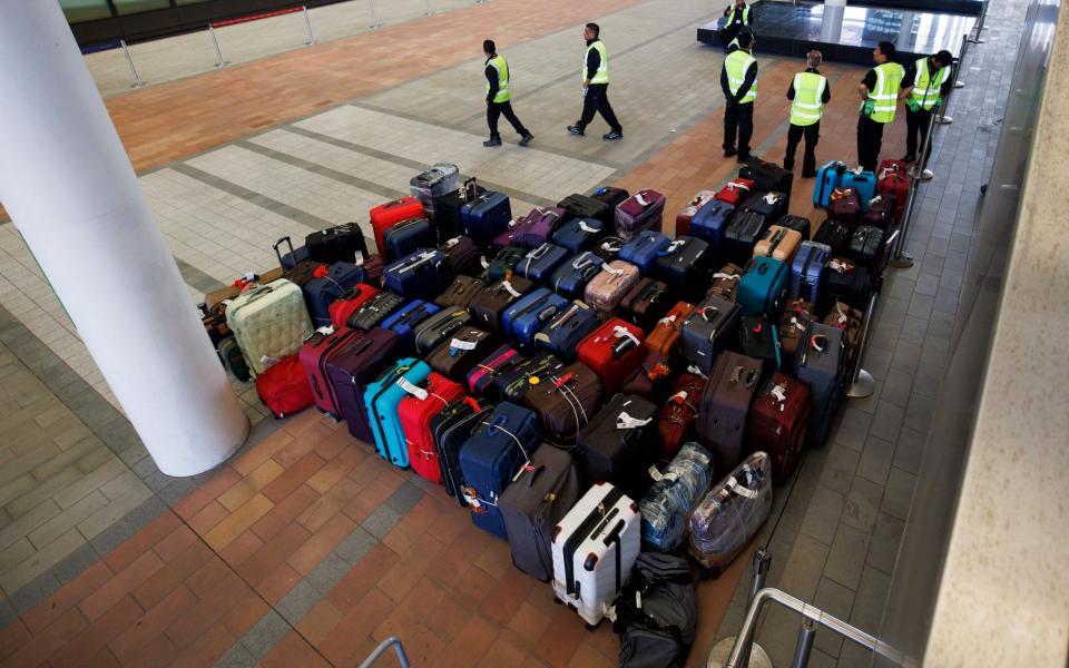 Baggage handlers load suitcases from a pile outside the entrance onto a DHL van at Heathrow's Terminal 2