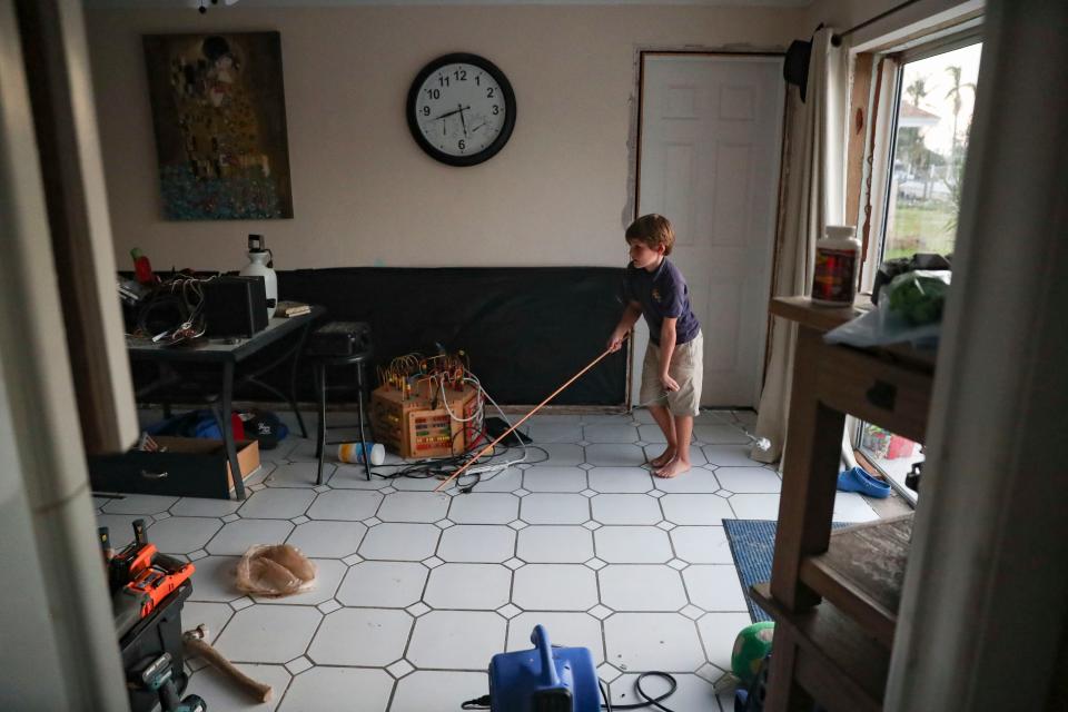 Luke Collins, 8, plays with a cat toy inside their home in Cape Coral on Monday, Dec. 12, 2022. Behind him is plastic attached to the wall after the lower portion was removed due to water damage.