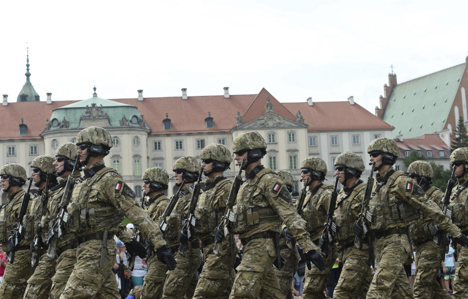 Polish Army soldiers salute as tanks roll on one of the city's main streets during a yearly military parade celebrating the Polish Army Day in Warsaw, Poland, Wednesday, Aug. 15, 2018. Poland marks Army Day with a parade and a call for US permanent military base in Poland. (AP Photo/Alik Keplicz)