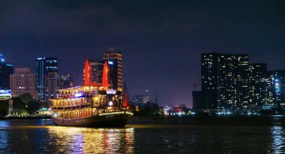 A cruise ship sailing along Saigon River, against the backdrop of tall buildings.