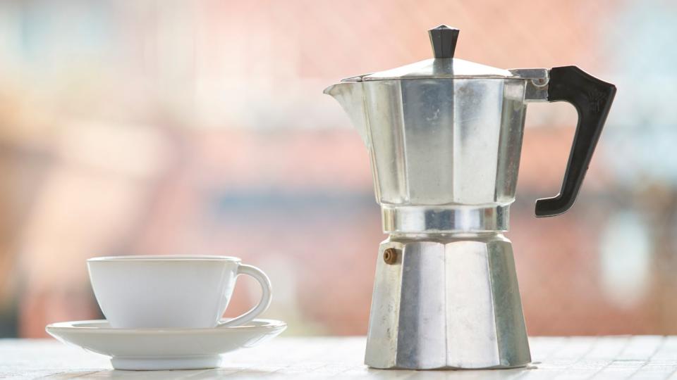 A stovetop coffee maker with a coffee mug on the left hand side