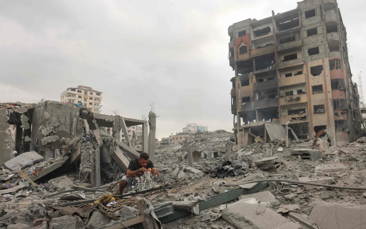 A Palestinian man washes his face from a damaged water pipe amid the rubble from Israeli airstrikes in Gaza City's al-Rimal neighbourhood