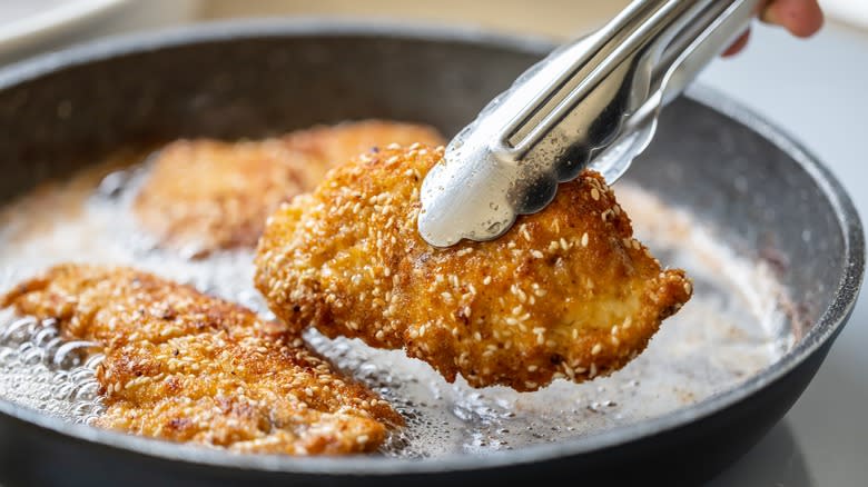 tongs with schnitzel, hot oil