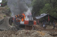 Gold miners stand next to a burning bulldozer set fire by National Police at an illegal gold mining operation as part of the Armed Forces' "Operation Guamuez III" in Magui Payan, Colombia, Tuesday, April 20, 2021. None of the workers were detained during the destruction of machinery, but in previous days some machinists and material suppliers were detained, according to Army Col. Pedro Pablo Astaiza. (AP Photo/Fernando Vergara)