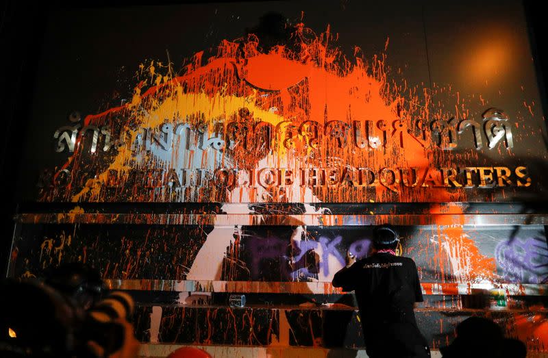 A person spray-paints the plaque with lettering in front of the police headquarters during a rally in Bangkok