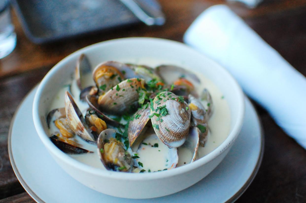 Clam chowder with whole clams and fresh herbs in a white bowl.