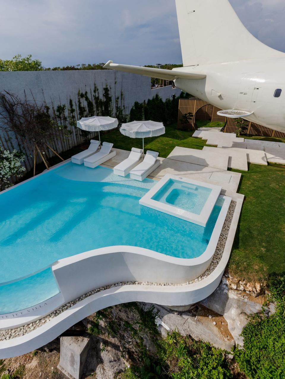 A pool sits next to a plane converted into a villa. It overlooks the beach.