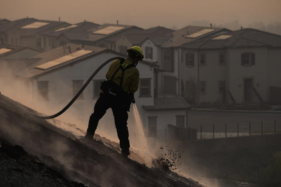 Firefighter Tylor Gilbert puts out hotspots while battling the Silverado Fire, Monday, Oct. 26, 2020, in Irvine, Calif. A fast-moving wildfire forced evacuation orders for 60,000 people in Southern California on Monday as powerful winds across the state prompted power to be cut to hundreds of thousands to prevent utility equipment from sparking new blazes. (AP Photo/Jae C. Hong)