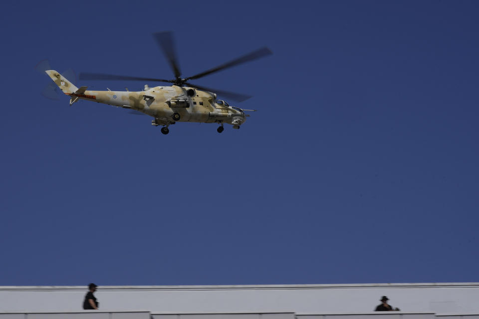 A military helicopter of Cypriot air force flies over two guard officers on a building, during a military parade marking the 62th anniversary of Cyprus' independence from British colonial rule, in divided capital Nicosia, Cyprus, Saturday, Oct. 1, 2022. Cyprus gained independence from Britain in 1960 but was split along ethnic lines 14 years later when Turkey invaded following a coup aimed at uniting the island with Greece. (AP Photo/Petros Karadjias)