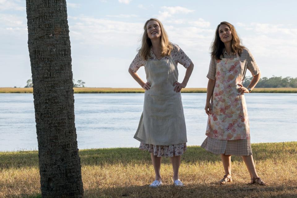 Julianne, on the left, standing next to Natalie with a body of water behind them in a scene from "May December". They are both wearing aprons