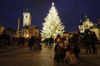 People gather by a Christmas tree illuminating the Old Town Square in Prague, Czech Republic, Saturday, Nov. 28, 2020. Prague city hall has lit up the Christmas Tre but cancelled the traditional Christmas markets due to a record surge in coronavirus infections. (AP Photo/Petr David Josek)