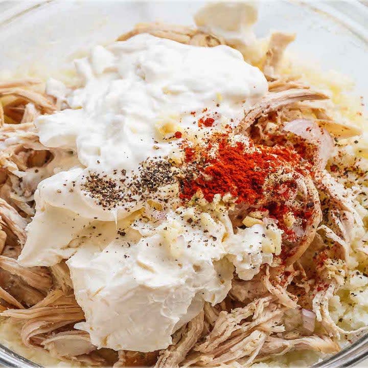 Shredded chicken mixed with cream cheese, sour cream, and spices in a bowl