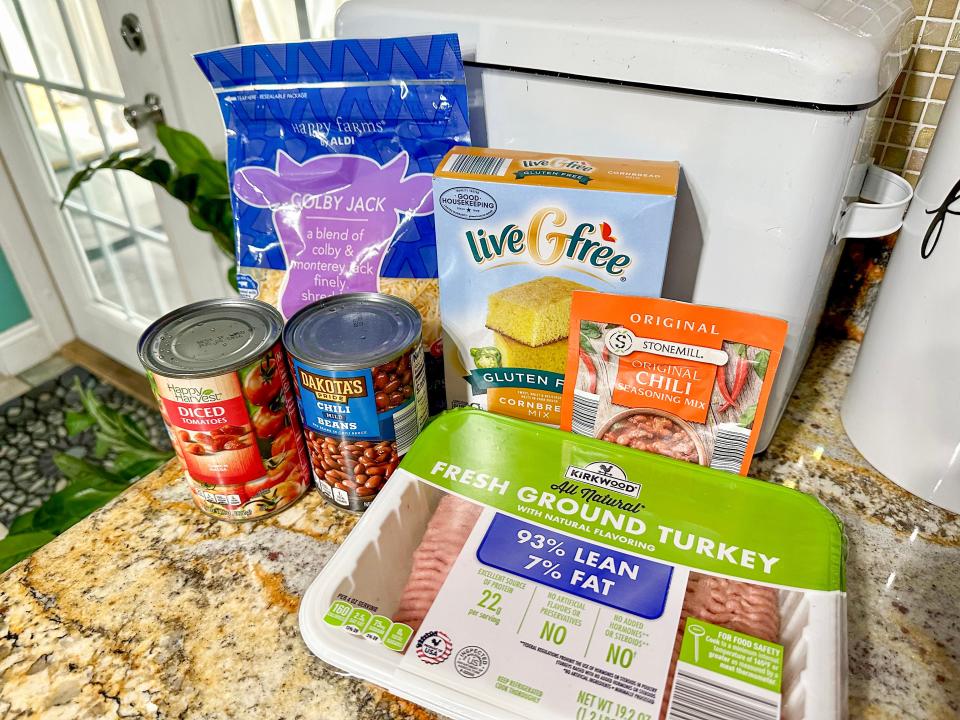 A counter with Kirkwood ground turkey, chili beans, diced tomatoes, a chili seasoning packet, liveGfree cornbread mix, and a bag of colby jack