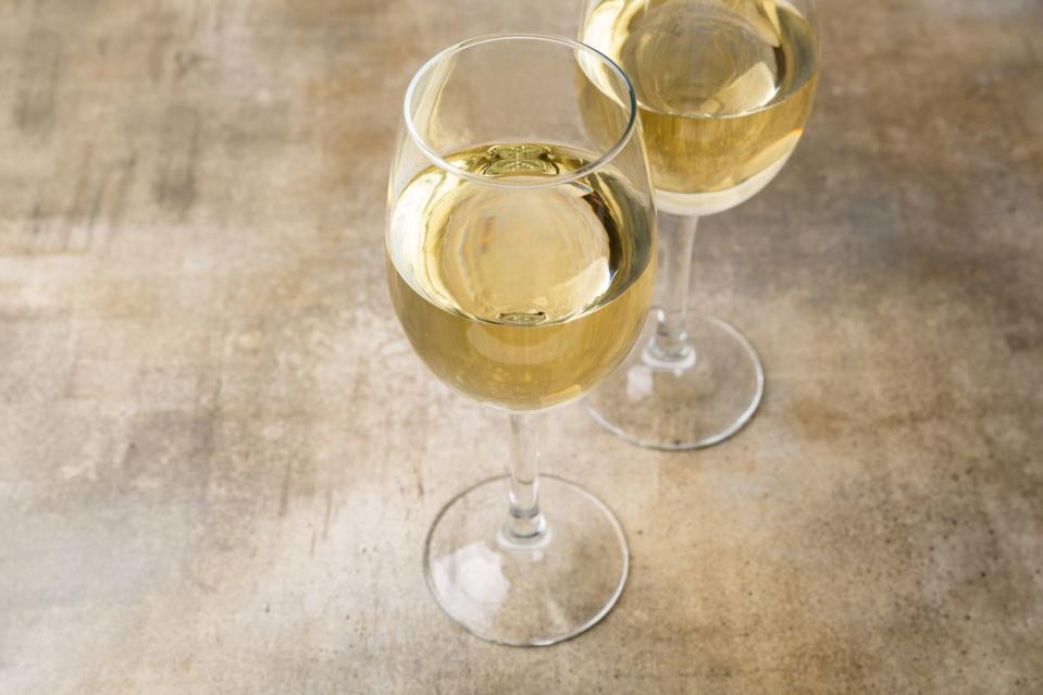 two glasses of white wine wine glasses over a brown background