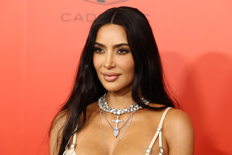 Kim Kardashian at a red carpet event, wearing a fitted, sleeveless outfit with layered, sparkling diamond necklaces