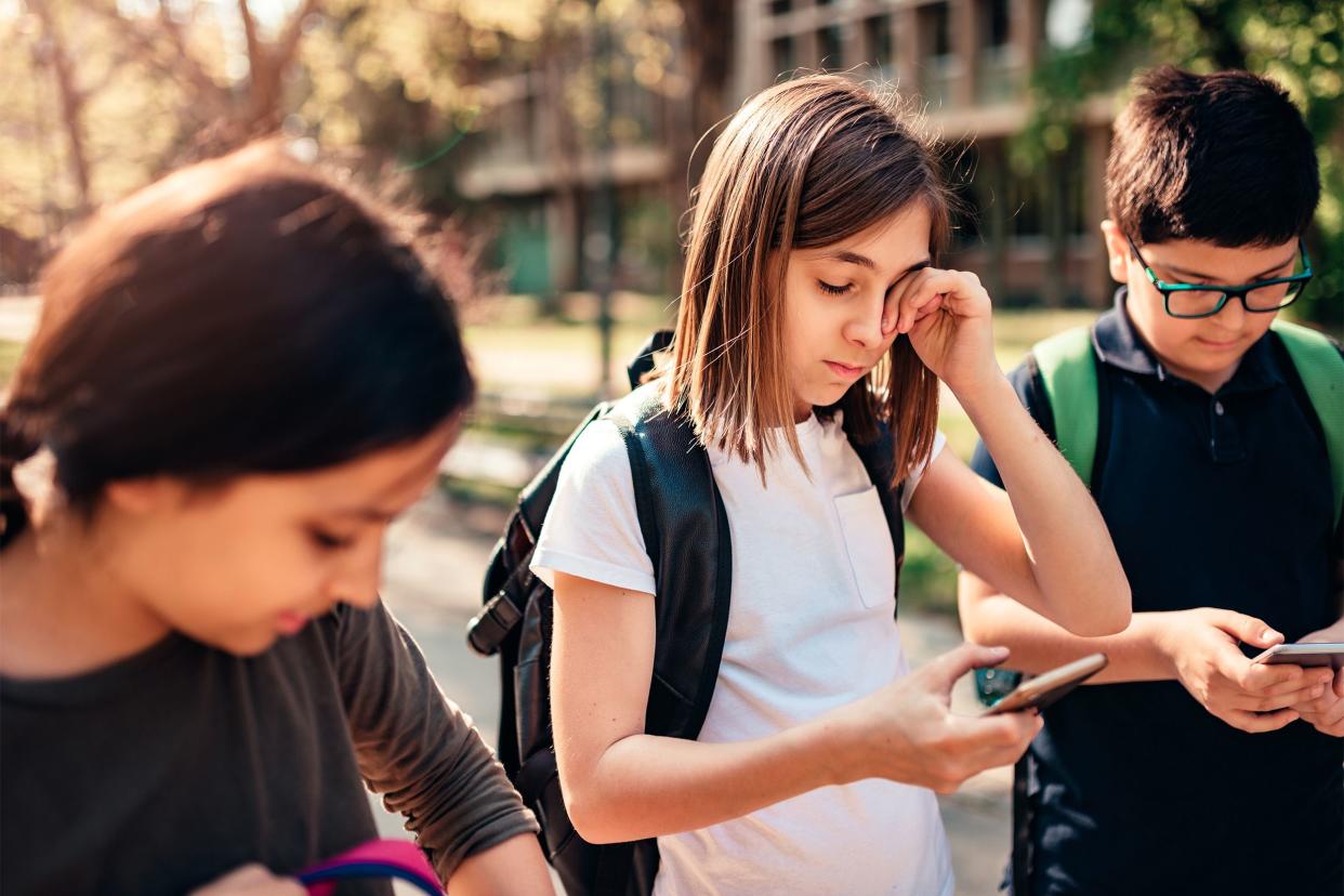 Girl touching her eye with kids on their phones walking home from school