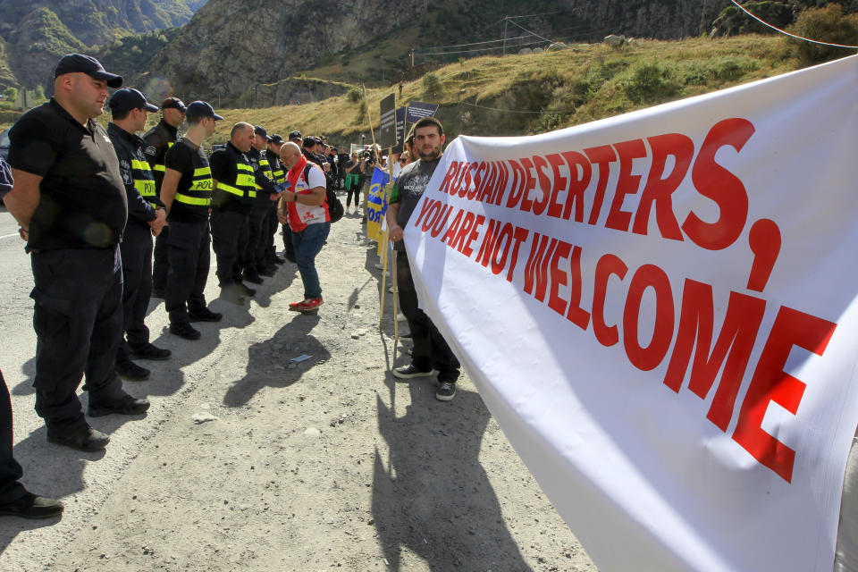 Georgian police form a line in front of activists holding an anti-Russian banner during an action organized by political party Droa near the border crossing at Verkhny Lars between Georgia and Russia in Georgia, Wednesday, Sept. 28, 2022. Protesters come from Tbilisi to voice their concerns over the exodus of Russian citizens into Georgia, that has increased since Vladimir Putin announced partial mobilization. (AP Photo/Shakh Aivazov)