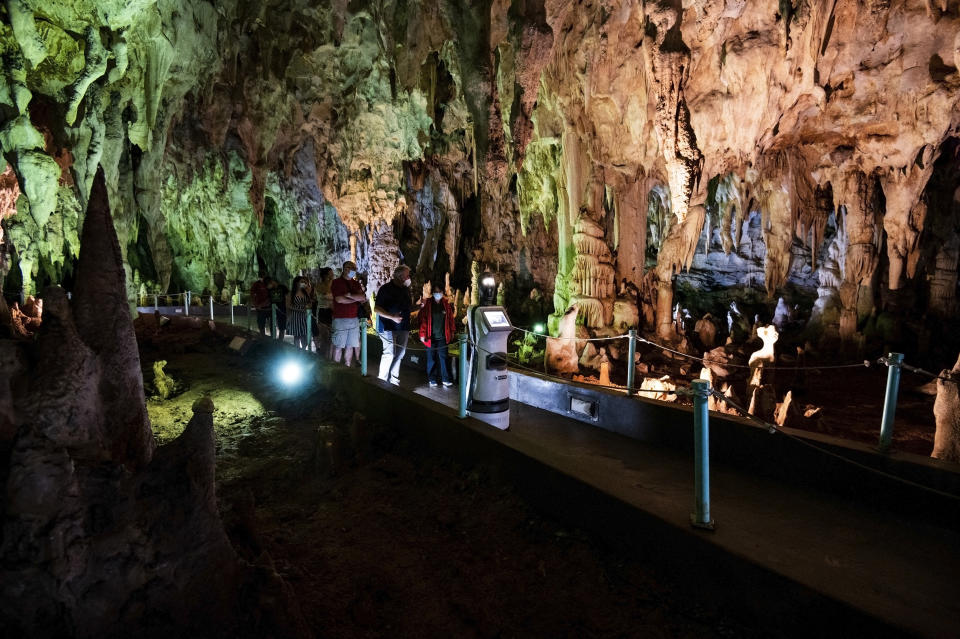 Persephone guides the visitors inside Alistrati cave, about 135 kilometers (84 miles) northeast of Thessaloniki, Greece, Monday, Aug. 2, 2021. Persephone, billed as the world's first robot used as a tour guide inside a cave, has been welcoming visitors to the Alistrati cave, since mid-July. (AP Photo/Giannis Papanikos)