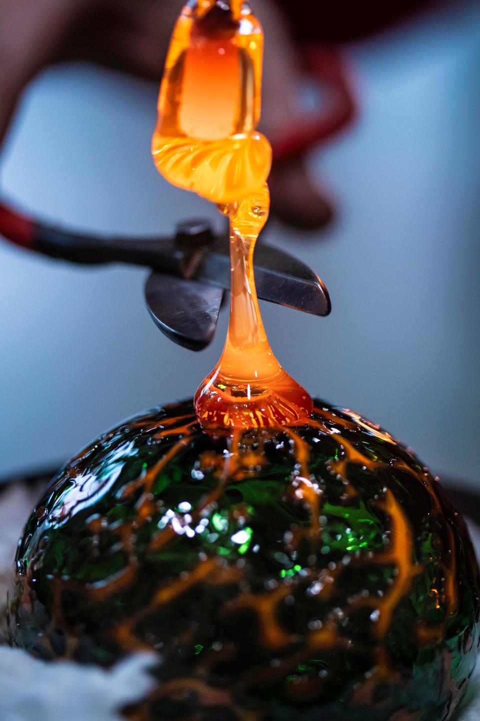 Molten glass is shaped to make a top for hanging an ornament inside the Glassworks’ Flame Run studio space on Friday. Dec. 15, 2018