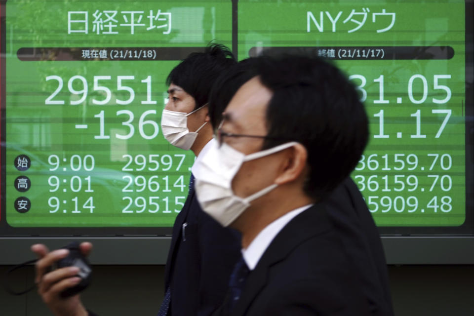 Men wearing protective mask walk near an electronic stock board showing Japan's Nikkei.