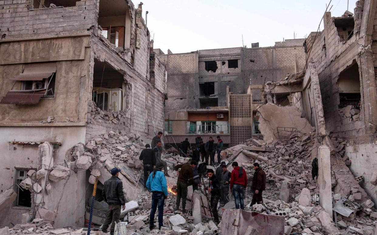 Syrian civil defence volunteers and other civilians attempt to remove rubble from the site of a collapsed building to rescue victims in Eastern Ghouta - AFP