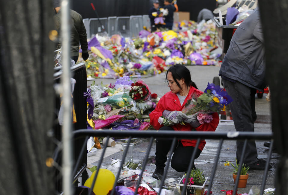 A workers picks up flowers amid thousands of items left in honor of Kobe Bryant, including hundreds of basketballs, from Chick Hearn Court from Staples Center, home of the Los Angeles Lakers, early Monday, Feb. 3, 2020, in Los Angeles. Mourners left the items after the death of the former Lakers legend, his daughter and seven others, in a helicopter crash one week ago.(AP Photo/Reed Saxon)