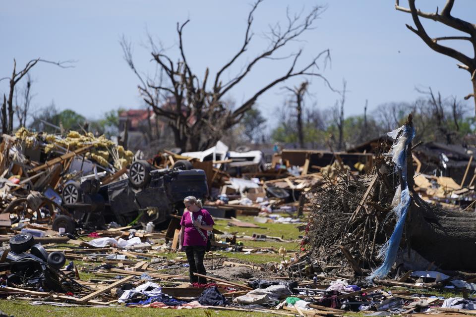 FILE - A woman walks near an uprooted tree, a flipped vehicle and debris from homes damaged by a tornado, March 27, 2023, in Rolling Fork, Miss. A new study says warming will fuel more supercells or tornados in the United States and that those storms will move eastward from their current range. (AP Photo/Julio Cortez, File)